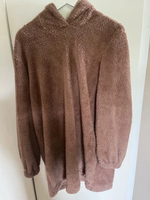 Brun fluffig hoodie i teddy-material - Mysig oversized hoodie i mjukt, fluffigt teddy-material i en varm brun färg. Hoodien har huva och långa ärmar med resår vid ärmsluten. Perfekt för dig som vill ha något riktigt bekvämt och stilrent till vardags. Inga synliga loggor eller märken.