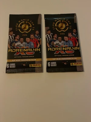 Panini Adrenalyn FIFA samlarkort - Två oöppnade paket Panini Adrenalyn FIFA Club World Cup 25 samlarkort. Varje paket innehåller 6 officiella trading cards med fotbollstema. Svart och guld design med spelarmotiv på framsidan. Perfekt för samlare eller fotbollsintresserade.