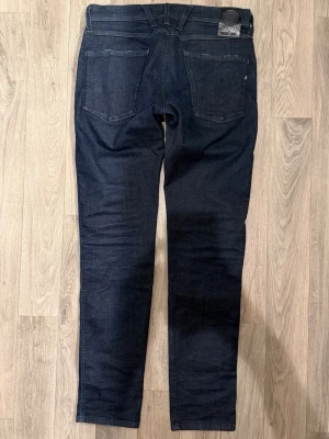 Replay Anbass Hyperflex Dry Jeans Mörkblå W31/L32 - Slim Fit - Replay Anbass Hyperflex Dry mörkblå jeans i stretchig Hyperflex denim med slim fit passform som sitter snyggt och bekvämt och funkar till allt, storlek W31/L32, midja 40 cm, ytterbenslängd 101,5 cm, benöppning 15,5 cm, modellen är 185cm & väger 65kg, i fint skick.