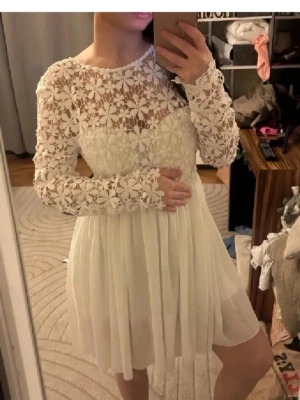 Studentklänning❤️ - Superfin vit kortklänning med långärmade spetsdetaljer och blommigt mönster upptill. Kjolen är lätt och luftig med plisserad känsla. Perfekt för sommarens alla tillfällen. Söt och romantisk look!