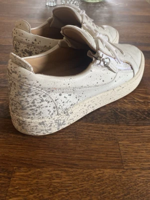 Giuseppe zanotti skor - Unika vita sneakers med snörning och dragkedja på sidan. Skorna har ett stänkmönster i grått och är tillverkade i skinn. Snygga skor i bra skick. Perfekta att ha nu inför sommaren! Skriv om ni har frågor