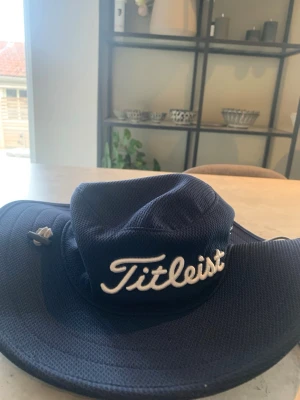 Mörkblå golf hatt från Titleist - Snygg mörkblå golf hatt från  Titleist med bred brätte och broderad vit logga framtill. Hatten är tillverkad i ett ventilerande meshmaterial som passar perfekt för golf eller andra utomhusaktiviteter.