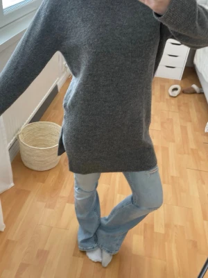 Mörkgrå oversized stickad tröja - Mysig mörkgrå stickad tröja i oversized modell med långa ärmar och slitsar i sidorna. Tröjan har en enkel, stilren design och är perfekt att bära till jeans. Materialet är mjukt och värmande, troligen ull- eller ullblandning.