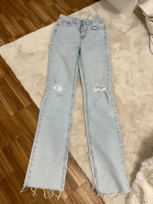 Ljusblå slitna jeans med slits - Trendiga ljusblå jeans med raka ben, slitningar vid knäna och råa, fransiga benslut med slits på sidorna. Klassisk femficksmodell i denim, perfekt för en avslappnad streetstyle-look.