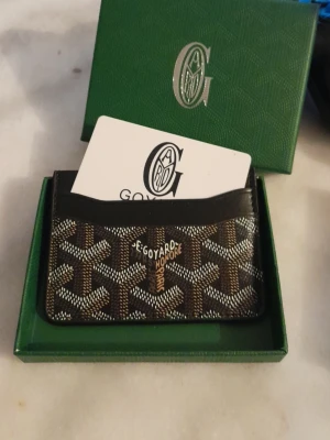 Svart/brun kortfodral i läder - Snyggt kortfodral  i brunt och svart med det klassiska mönstret. Tillverkat i läder med flera fack för kort. Kommer i original grön ask med logga. Perfekt för dig som vill ha något stilrent och exklusivt i fickan.