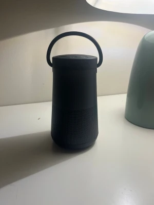 Bose svart bärbar Bluetooth-högtalare - Snygg svart bärbar högtalare från Bose med rundad cylinderform och praktiskt bärhandtag. Högtalaren har perforerat metallgaller runt om för 360° ljud och en stilren, modern design. Perfekt för att ta med sig överallt och enkel att koppla upp via Bluetooth orginal pris 3,500kr så jag säljer den för billigare för 1,500kr