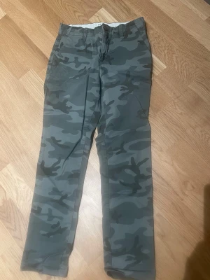 Camo chinos från GAP - Snygga chinos från GAP i girlfriend-modell med grågrönt camomönster. Byxorna har raka ben, klassiska fickor och är tillverkade i ett mjukt bomullsmaterial. Perfekta för dig som vill ha en avslappnad men trendig look.