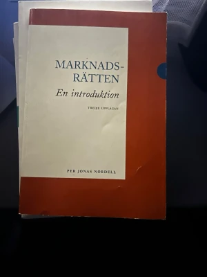 Marknadsrätten: En introduktion - Kursbok i marknadsrätt, tredje upplagan, skriven av Per Jonas Nordell. Omslaget är vitt och rödbrunt med blå text. Perfekt för dig som pluggar juridik eller ekonomi och behöver en tydlig introduktion till marknadsrättens grunder.