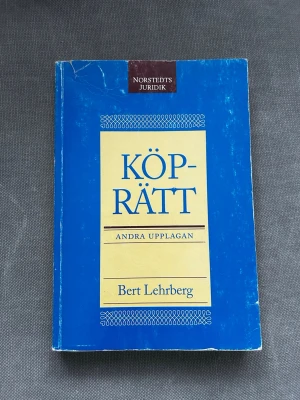 Köprätt av Bert Lehrberg - Kursbok i köprätt, andra upplagan, skriven av Bert Lehrberg. Omslaget är blått med en gul rektangel och blå text. Perfekt för juridikstudier och fördjupning i avtals- och köprätt. Mjukpärm och tydlig layout.