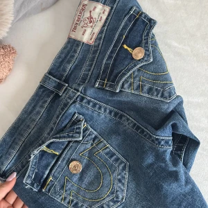 Blå bootcut jeans från true religion  - Snygga blå jeans från true religion med klassisk bootcut passform. Jeansen har fem fickor, gylf med dragkedja och knapp samt kontrastsömmar. Tillverkade i slitstarkt denimtyg som ger en tidlös look.