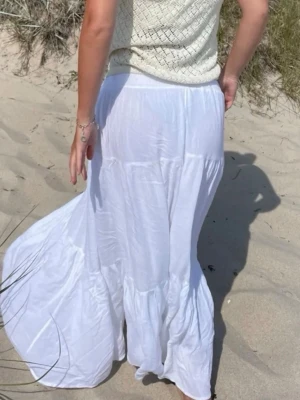 Vit långkjol - Säljer en flowy vit långkjol i tunn bomull med volangdetaljer. Kjolen har en avslappnad passform och är perfekt för varma dagar. Enkel och stilren design som passar till många olika toppar. Storlek 36