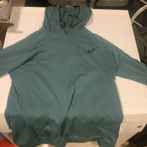 Blågrön hoodie från MyProtein - Snygg blågrön hoodie från MyProtein med diskret logga på bröstet. Hoodien har huva med dragsko och långa ärmar. Tillverkad i mjukt material som känns skönt mot huden. Gymtröja, träningskläder träningshoodi