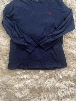 tröja Ralph Lauren - Klassisk mörkblå långärmad tröja från Polo Ralph Lauren i mjuk bomull. Tröjan har rund halsringning och den ikoniska röda logotypen broderad på bröstet. Perfekt för en clean och stilren look.