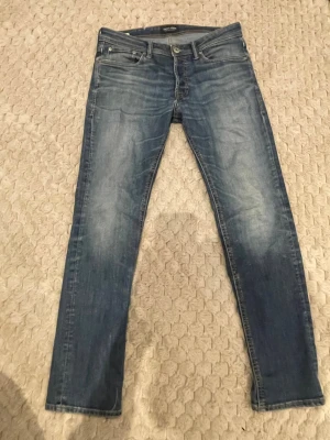 Blå slim fit jeans från Jack & Jones - Snygga blå slim fit jeans från Jack & Jones med klassisk femficksdesign och slitna detaljer framtill. Jeansen har normal midja och smala ben, perfekta till en avslappnad stil. Tillverkade i bomull med lite stretch för extra komfort.