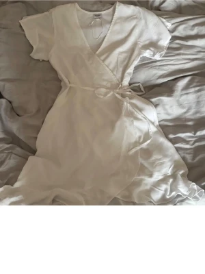 Studentklänning - Studentklänning med knyt i midjan och volangdetaljer längs nederkanten. Klänningen har korta ärmar och v-ringad hals. Använd 2 ggr på studenten. Passar också som small.