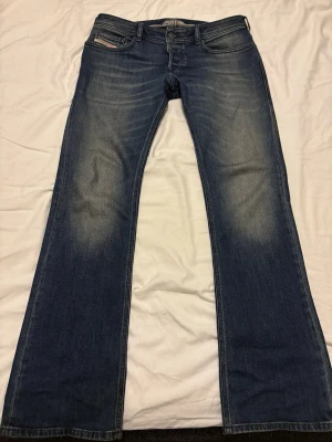 Blå bootcut jeans från Diesel - Säljer ett par blå bootcut jeans från Diesel med klassisk femficksdesign och snygga slitningar på framsidan. Jeansen har en låg midja och är tillverkade i denim med en skön stretch. Perfekta för dig som gillar en avslappnad och trendig look. W32 L32, ej fast pris lägg bud.