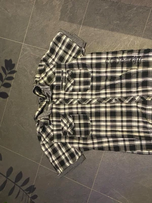 Svartvit rutig skjorta från jack and Jones  - Kortärmad skjorta från Jack and Jones i svartvitt rutigt mönster. Skjortan har två bröstfickor med lock och knappar, samt broderad logga på bröstet. Tillverkad i mjuk bomull och har klassisk krage och knappstängning framtill.