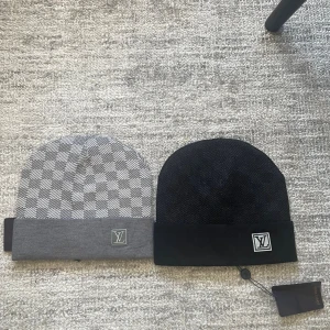 Louis Vuitton mössor svart & grå - Två snygga mössor från Louis Vuitton, en i svart och en i grått med rutigt mönster. Båda har LV-logga framtill och är ribbade vid kanten. Perfekta accessoarer för att lyfta din outfit. Kostar 300kr styck eller 500 för båda 