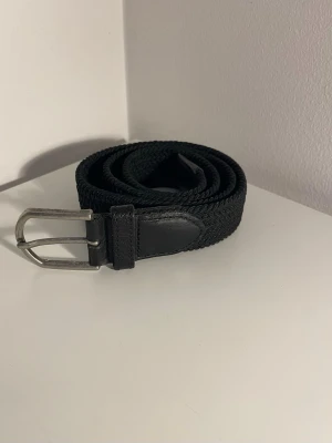 Svart flätat bälte - Stilrent svart bälte med flätad design och detaljer i skinn. Metallspänne i silverfärg ger en klassisk look. Storlek: 80 