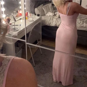 Ljusrosa långklänning  - Säljer en elegant ljusrosa långklänning med smala axelband. Klänningen har en figurnära passform och är tillverkad i ett mjukt, stretchigt material som ger en smickrande siluett.