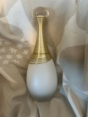J'adore parfymflaska från Dior - Elegant parfymflaska från Dior, J'adore, med matt vit kropp och guldfärgad hals i spiralform. Locket är klotformat i transparent plast med ingraverad text. Flaskan har en lyxig och feminin design som verkligen sticker ut på sminkbordet. Ny pris är ca 1300 använt den lite så de är ca 40 ml kvar. 