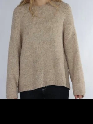 Beige stickad tröja i ullmix - Mysig beige stickad tröja med rund hals och långa ärmar. Tröjan har en rak passform och är tillverkad i en mjuk ullmix som känns skön mot huden. Perfekt för lager på lager och enkel att matcha med olika stilar.