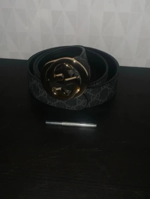 Svart Gucci skärp med GG-spänne - Snyggt svart skärp från Gucci med klassiskt GG-mönster och stort guldfärgat GG-spänne. Skärpet är gjort i skinn och har en exklusiv känsla som lyfter vilken outfit som helst. Perfekt accessoar för dig som gillar lyxiga detaljer.