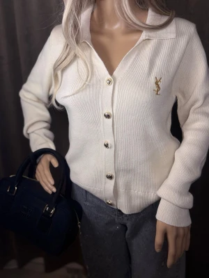 Vit cardigan  -  Tröjan har ribbad struktur, klassisk krage och långa ärmar. Perfekt för dig som gillar exklusiva och tidlösa plagg.