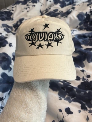 Beige tjuvjakts keps - Säljer en beige keps med justerbar rem bak och ett coolt svart tjuvjakts tryck och stjärnor. Kepsen har böjd skärm och är tillverkad i bomullstyg. Perfekt för dig som vill ha en unik och trendig accessoar. Kepsen är köpt på tjuvjakts konsert på hovet och är oanvänd💕