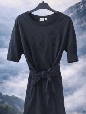 Svart kort klänning med knytband - Svart kort klänning från .object med rund halsringning och knytband i midjan. Klänningen har korta ärmar och är tillverkad i mjuk bomull, vilket gör den bekväm och enkel att bära. Perfekt för en avslappnad och stilren look.