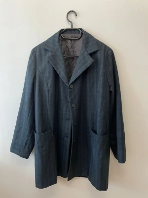 Blå rutig oversized kavaj - Blå grön kavaj med diskret rutmönster och figursydd passform. Kavajen har breda slag och stora fickor. Materialet känns som en klassisk kostymullblandning.