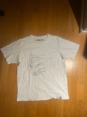 Vit Star Wars t-shirt från Uniqlo - Vit t-shirt från Uniqlo UTGP 2015 med minimalistiskt Stormtrooper-tryck och texten 'Star Wars 1977' på framsidan. Bra skick och i storlek large 