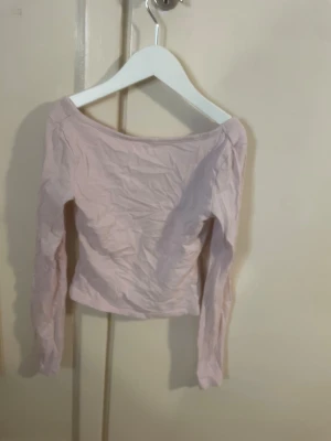 Ljusrosa offshoulder topp med halvt öppen rygg - Säljer en ljusrosa offshoulder topp med lång ärm och croppad passform. Toppen är enkel och stilren, perfekt att matcha med jeans eller kjol. Materialet känns mjukt och lätt, troligen bomull eller en bomullsblandning.