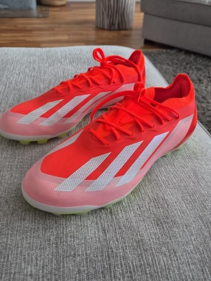 Adidas Crazyfast röda fotbollsskor - Säljer ett par Adidas Crazyfast fotbollsskor i rött med vita detaljer och snörning. Skorna har en lätt syntetisk ovandel och dobbar i vitt och gult för bra grepp på planen. Perfekta för dig som vill ha speed och stil på fotbollsplanen.