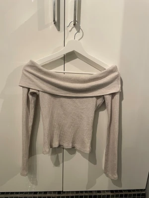 Beige offshoulder ribbad topp - Trendig beige offshoulder topp med långa ärmar och ribbad struktur. Perfekt för dig som vill ha en stilren och enkel look med en twist. Är lätt att matcha med både jeans och kjol.