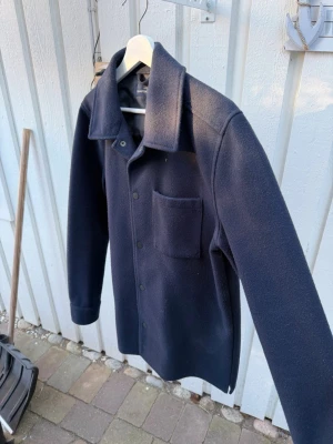 Mörkblå tjock overshirt från Hamtons republic - Stilren mörkblå overshirt från  Hamtons Republic i tjocka ullmix material. Perfekt lager-på-lager-plagg för kyligare dagar och enkel att matcha med olika outfits. Tveka inte på att höra av dig vid eventuella frågor!