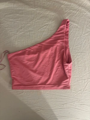 Rosa oneshoulder topp - Trendig rosa oneshoulder topp i mjukt material. Perfekt för dig som vill sticka ut med en enkel men snygg look. Toppen är ärmlös och har en asymmetrisk axel, vilket ger en cool vibe.