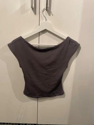 Mörkgrå ribbad croppad topp - Säljer en mörkgrå croppad topp med ribbad struktur. Toppen är en rygglösmodell, vilket ger en snygg och modern look. Perfekt att matcha med höga jeans eller kjol för en trendig outfit.