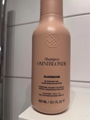 Omniblonde Rejuvenation Shampoo - Beige flaska med Omniblonde Rejuvenation Shampoo, 300 ml. Schampot är färgsäkert och har pH 5,5-6,5. Det ger återfuktning, glans och är speciellt framtaget för blont hår. Flaskan har en stilren, rundad form och är tillverkad i plast.
