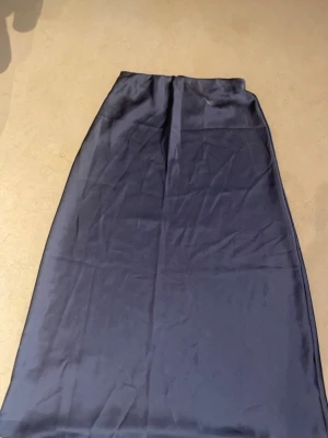 Grå Satin Kjol - Grå sarin kjol med töjbart band runt midjan 🩶 Den är lång och täcker strax ovanför fötterna. Har använt 1-2 gånger MAX, så den är nästan helt ny. Vet ej vilket märke det är :( då jag fick den som present. Den är i storlek XS men funkar för dig som är S också 🫶🏼