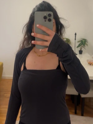 Mörk grå croppad bolerotopp Gina tricot  - Säljer en mörk grå croppad bolerotopp med lång ärm. Toppen har en enkel och stilren design som passar perfekt till olika outfits. Materialet känns mjukt och stretchigt, vilket gör den bekväm att bära. Perfekt för dig som vill ha en trendig layering-look.