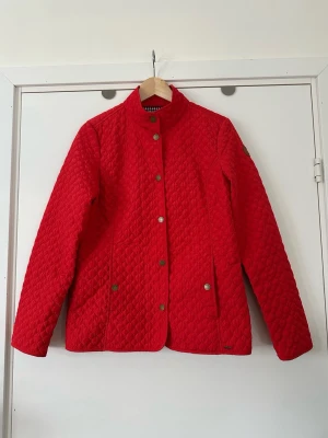 Röd quiltad Luhta jacka, storlek 40 - Kvalitativ röd quiltad jacka från Lutha med rutigt foder. Jackan har en ståkrage och knäppning framtill med tryckknappar. Det finns även fickor framtill med tryckknappar. Står storlek 36, men är storlek 40. En stilren jacka som passar för många tillfällen. Mycket gott skick, som ny!  Skickas mot porto, kan även hämtas i Stockholm. 