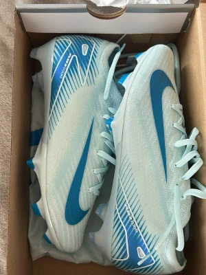 Nike Mercurial fotbollsskor blå/vit - Snygga Nike Mercurial fotbollsskor i ljusblått och vitt med blå detaljer och klassisk Swoosh-logga. Skorna har snörning. Använda 1 gång för dom va för små så dom är som helt nya. Storlek 38☺️ordinarie pris 2900kr 