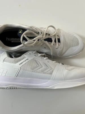 Vita Hummel Power Play Pro sneakers - Snygga vita sneakers från Hummel, modell Power Play Pro. Skorna har en sportig design med meshpaneler för extra ventilation och detaljer i syntetmaterial. Perfekta för inomhussport tack vare den greppvänliga sulan och bekväm passform.OBS! Varan har ett litet hål så vänligen se bild!
