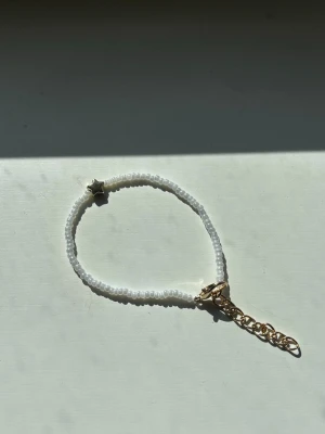 Vitt pärlarmband med stjärndetalj - Handgjort armband med små vita pärlor och en liten guldig stjärnformad detalj. Armbandet har en justerbar guldfärgad kedja. 