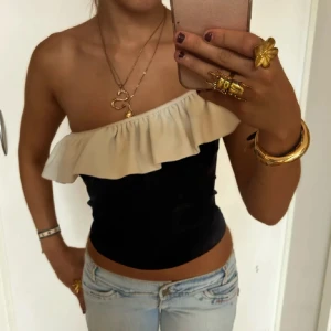 Svart och vit offshoulder topp - Trendig svart topp med vit volangdetalj i offshoulder-stil. Perfekt för en stilren look med en touch av elegans.