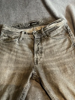 Grå jeans från Jack & Jones - Snygga grå jeans från Jack & Jones med klassisk femficksdesign och raka ben. Jeansen har en tvättad look och är tillverkade i bomull med en liten stretch för extra komfort. Perfekta för en avslappnad och trendig stil. Storlek: 28 30
