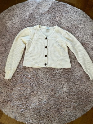 Vit stickad kofta med knappar - Snygg vit stickad kofta med långa ärmar och bruna knappar framtill. 