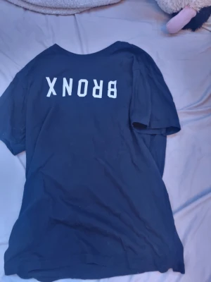 Svart t-shirt med BRONX-tryck från SOC - Svart t-shirt från SOC i storlek S med vitt tryck där det står 'BRONX' på ryggen. Klassisk rund hals och korta ärmar. Perfekt för en avslappnad streetwear-look.