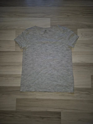 Gråmelerad t-shirt från H&M - En basic gråmelerad t-shirt från H&M med rund halsringning och korta ärmar. T-shirten har en enkel och stilren design, perfekt att matcha med jeans eller shorts. Tillverkad i mjuk bomull för en skön känsla hela dagen.
